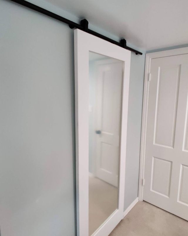 Same closet with a white mirrored sliding barn door on a black rail